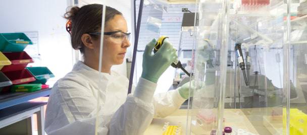 A Charles River scientist in a lab coat and safety glasses using a pipette at a laboratory workstation
