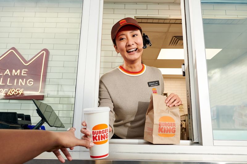 Smiling Burger King team member handing a branded bag and drink through the drive-thru window
