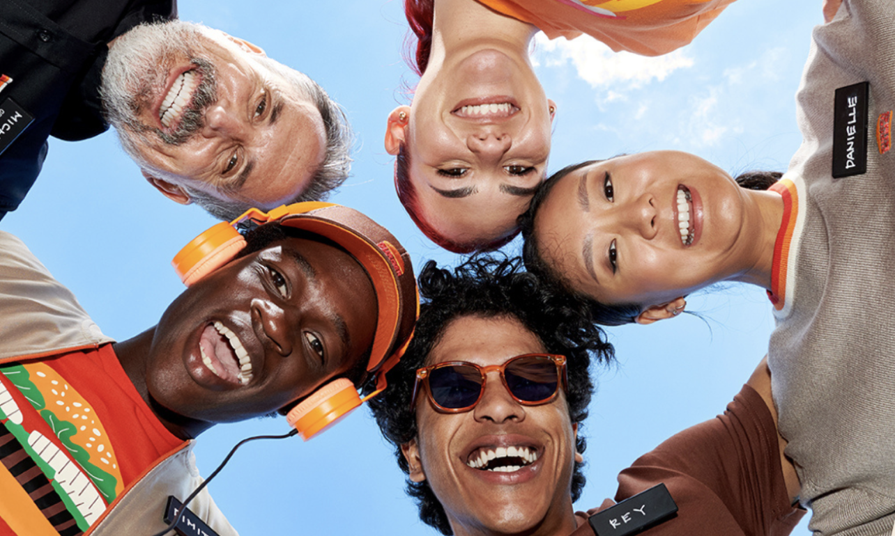 Five diverse Burger King team members smiling together in a close huddle under a blue sky