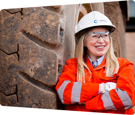 A smiling CRH worker in hi-vis gear beside heavy construction equipment