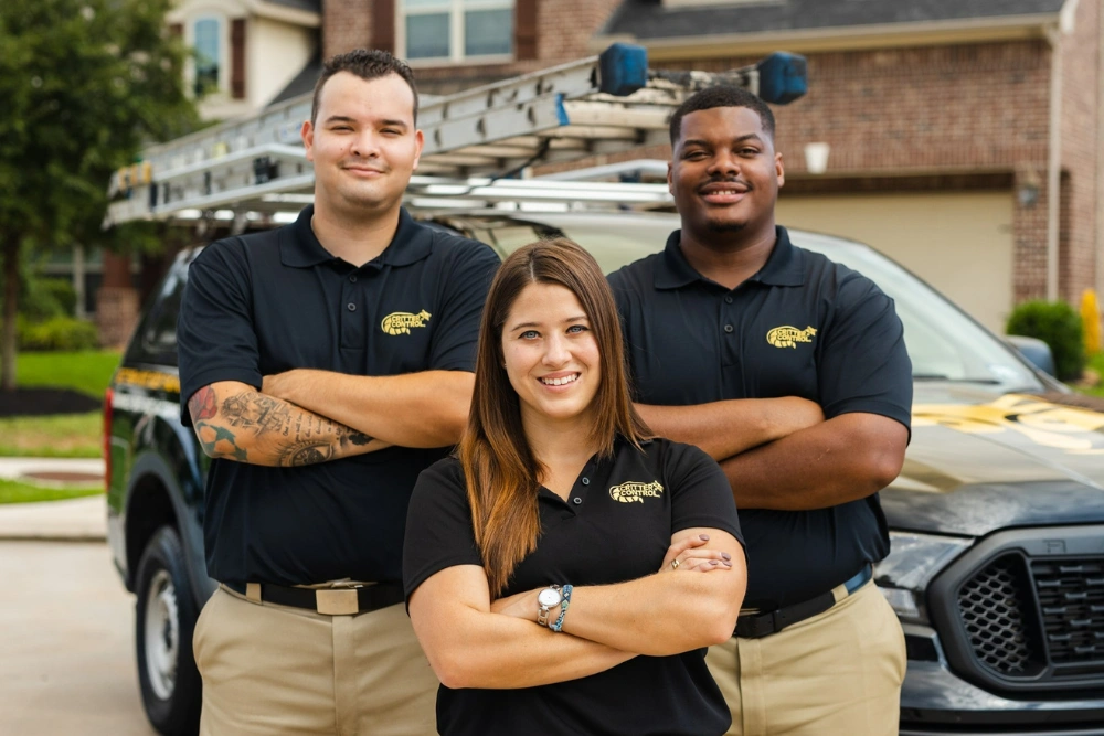 Three Critter Control wildlife technicians in branded polos standing in front of a company service truck