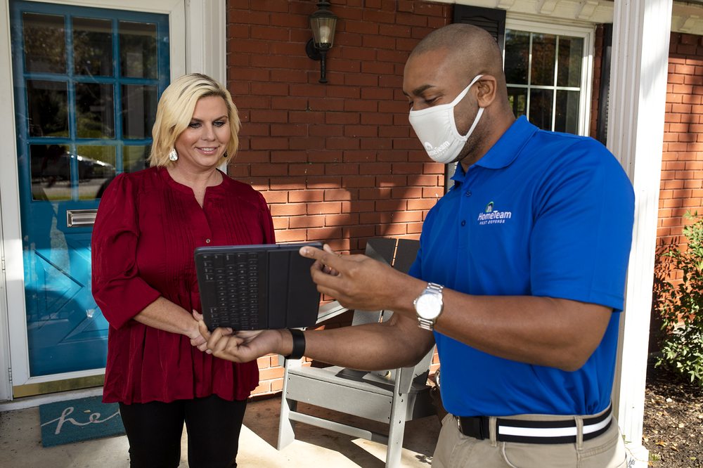 A HomeTeam Pest Defense technician reviewing a service plan with a homeowner on a front porch