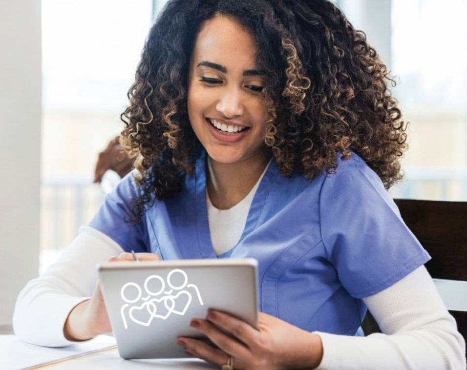 A smiling LHC Group clinician in scrubs charting patient care on a tablet