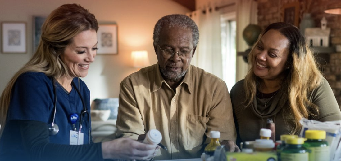An LHC Group home health nurse and a caregiver reviewing medications with a smiling elderly patient at home