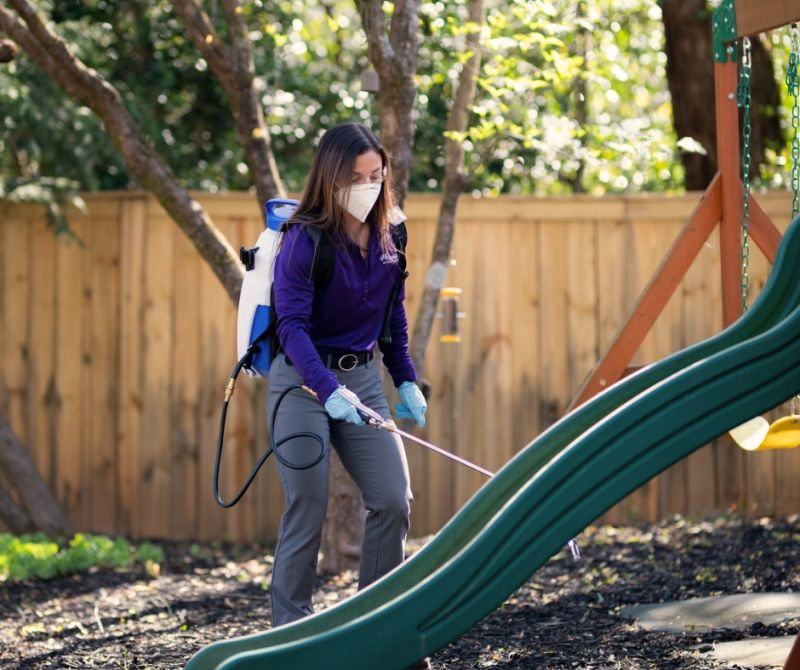 MissQuito field service technician treating a backyard near a children's play set