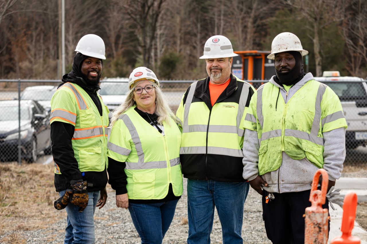 Four Thompson Arthur crew members in hi-vis vests and hard hats smiling together at a job site