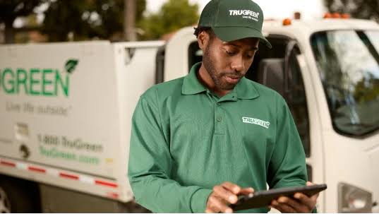 A TruGreen associate using a tablet beside a service truck