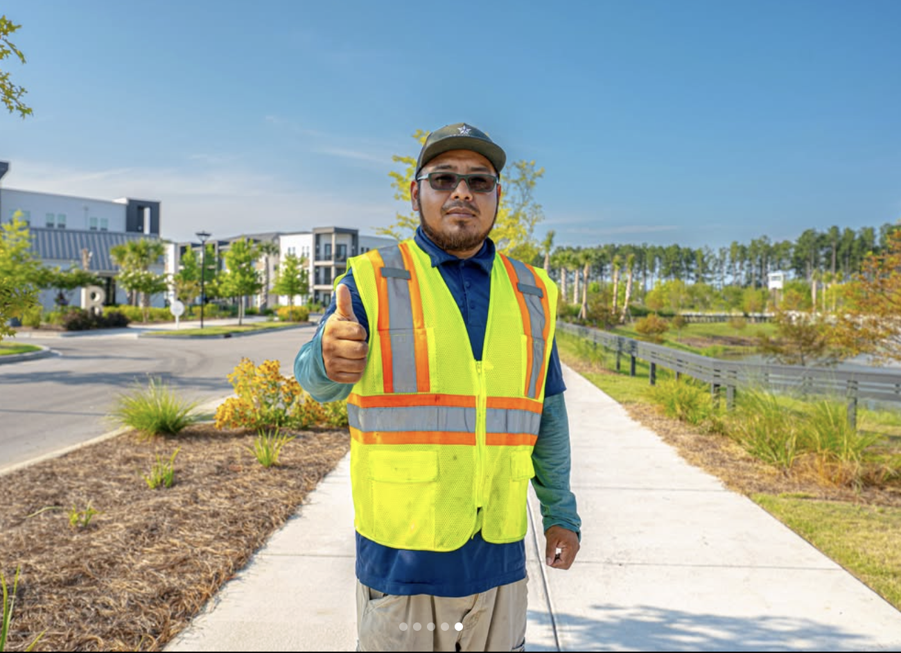 A Yellowstone Landscape crew member in a hi-vis safety vest giving a thumbs up on a commercial property walkway