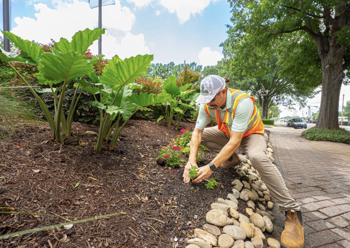A Yellowstone Landscape crew member in a hi-vis safety vest planting flowers in a commercial landscape bed