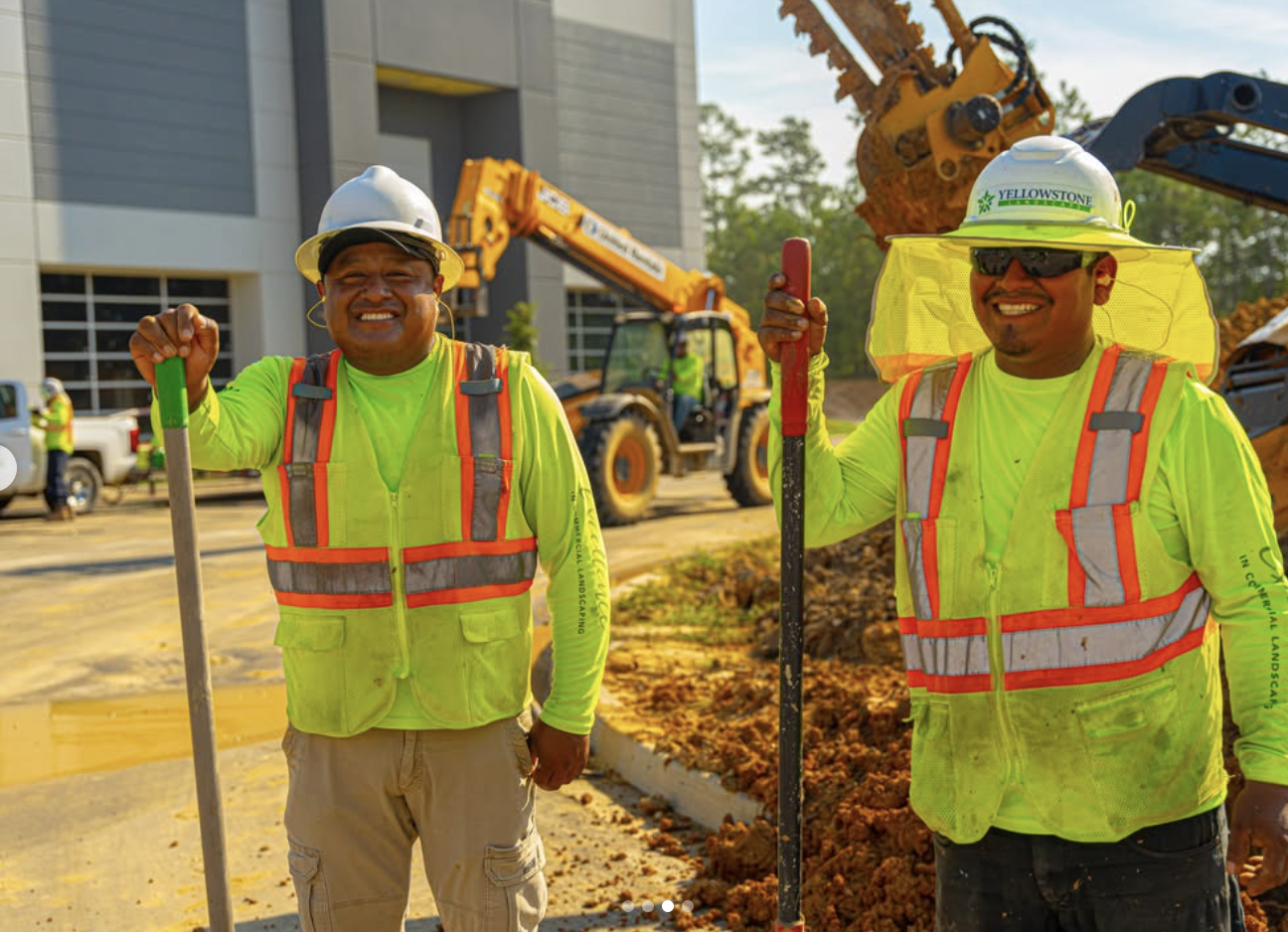 Two Yellowstone Landscape crew members in hi-vis gear with shovels at a commercial installation site
