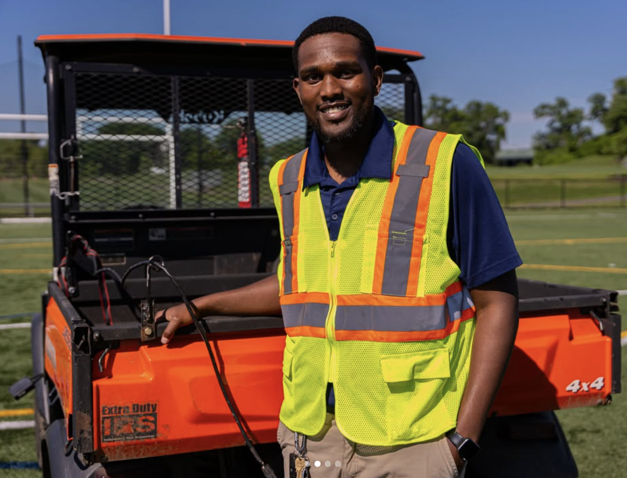 A Yellowstone Landscape team member in a hi-vis vest standing by a utility vehicle on a sports field