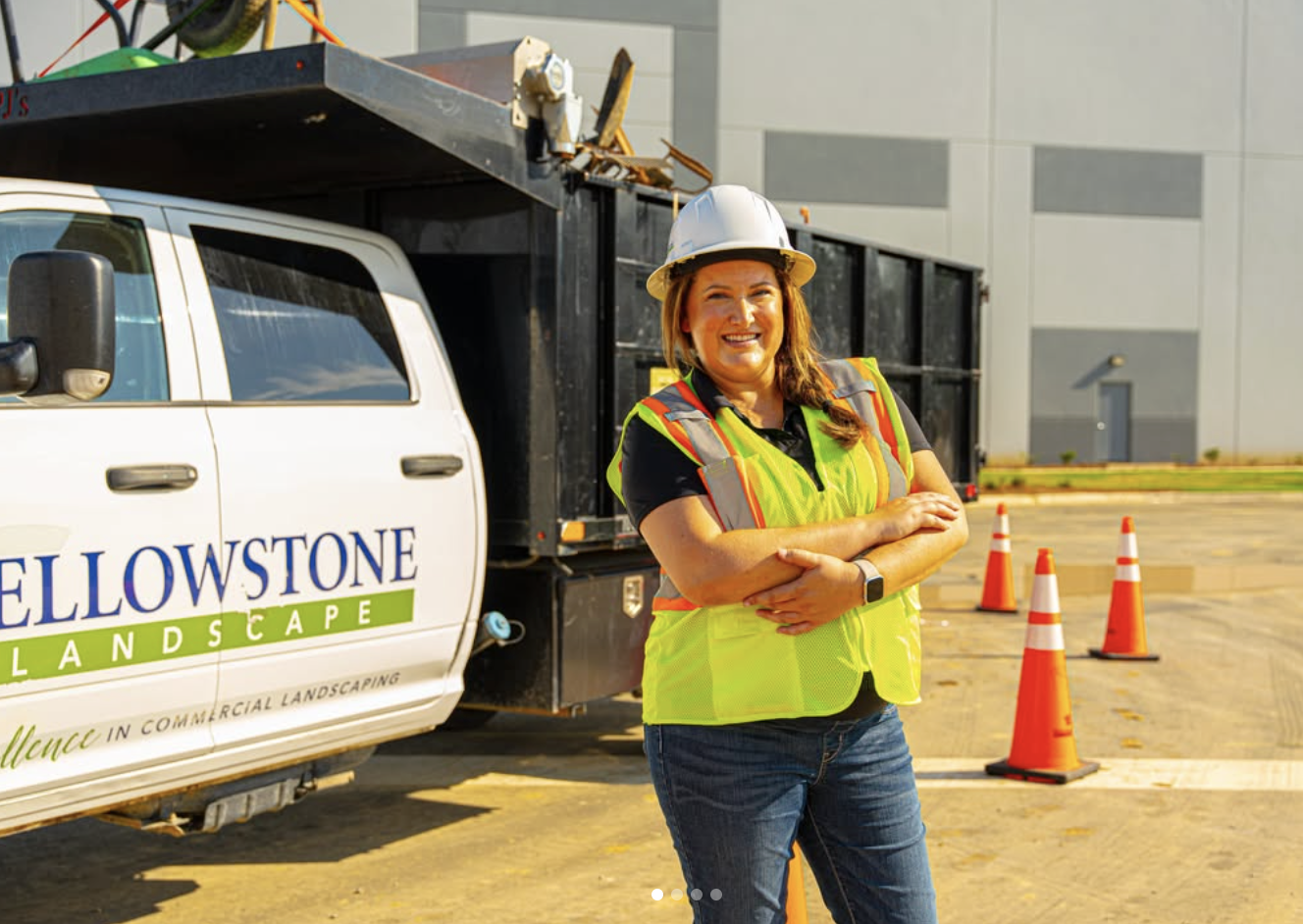 A Yellowstone Landscape team leader in a hard hat and safety vest smiling beside a company truck