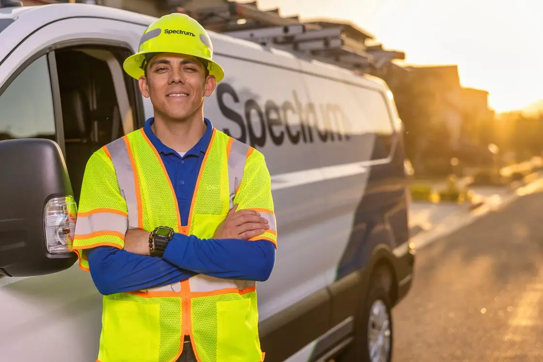 A Spectrum Field Technician in high-visibility gear standing in front of a Spectrum van