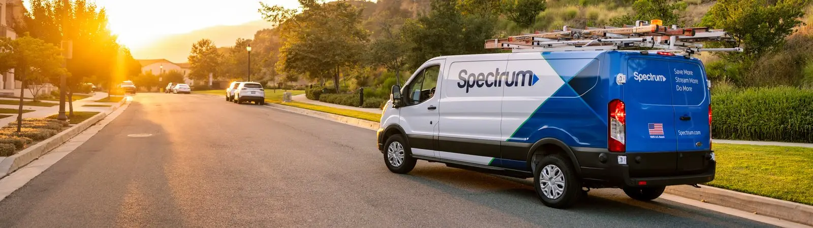 A Spectrum-branded field services van driving through a residential neighborhood at sunset