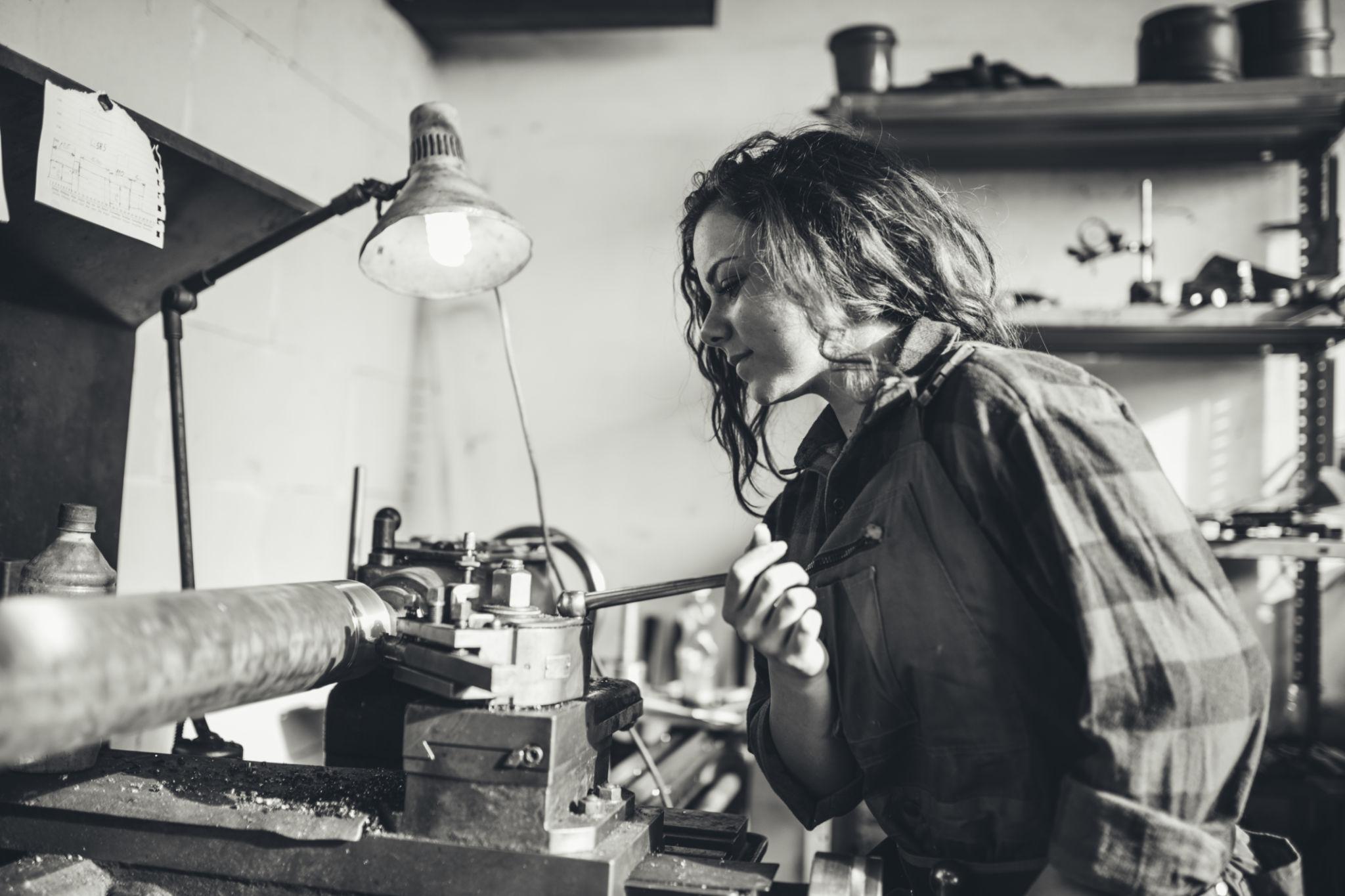 A young tradesperson working at a metal lathe in a workshop